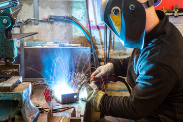 Worker in welding mask at factory. Welding process. Electric welding. Bright yellow sparks.