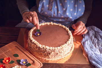 Female hands decorate home-made Kiev cake with sugar flowers.