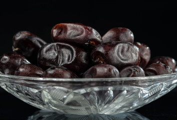 Crystal saucer with a bunch of dried dates on a dark mirror background.