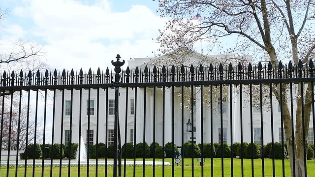 Loopable cinemagraph slow motion view through fence on White House in Washington DC, USA with fountain splashing water in spring by green grass lawn and American flag