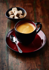 Cup of coffee and brown sugar cubes on rustic background. 