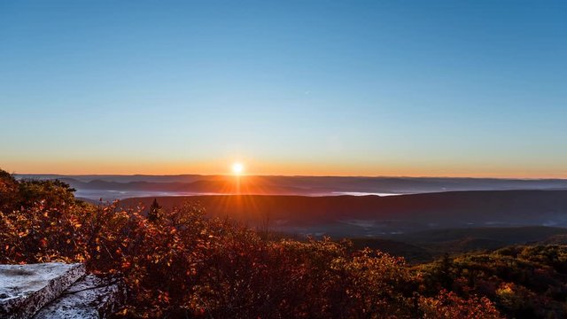 Loopable cinemagraph of timelapse, time lapse of Bear rocks overlook in Dolly Sods, West Virginia during dawn, sunrise in autumn, fall with rocky landscape trees, blue sky and sun behind mountains