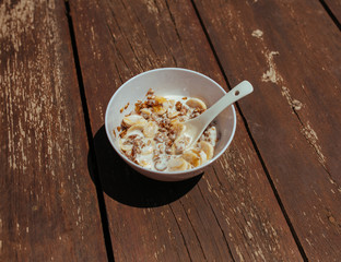 Muesli with banana in white bowl with spoon on a wooden bench