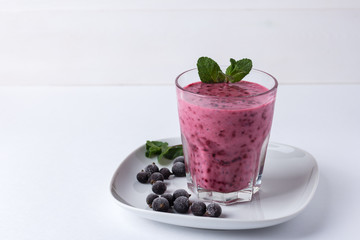 blackcurrant smoothie in a glass cup on a plate, on a white background, horizontal orientation,...