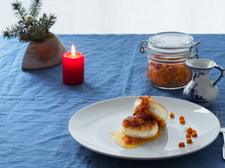 Cheesecakes or curd pancakes with cream and sea buckthorn jam on a white plate, on a blue tablecloth. Vintage gravy boat. Сandle. Homemade сottage cheese fritters. Tasty breakfast. Closeup.