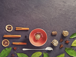 Chinese herbal tea twisted into a sphere of leaf is in a mug. Nearby are various spices (anise stars, cinnamon sticks, lemon slices, pomegranate flower petals, green leaves). Making a healthy drink.