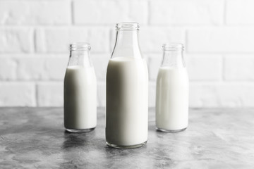 Three glass reusable bottles of milk in the kitchen with marble countertops and a white brick wall.