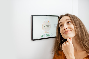 Portrait of a young happy woman near a touch screen panel for a smart home control. Concept of a simple and convenient application for managing smart devices at home