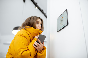 Young woman in winter clothes, feeling cold, waiting for the house to heat up, controlling heating...