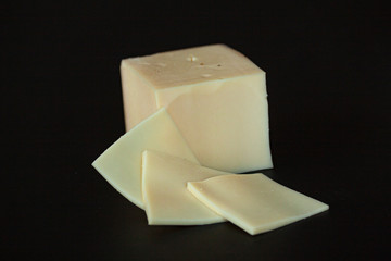 Slices of yellow cheese lying in front of a block of cheese on black background. Selective focus close up image.