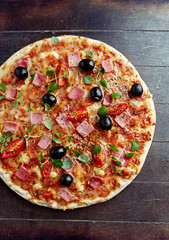 Pizza with ham, mozzarella cheese, cherry tomatoes, black olives and fresh oregano. Home made food. Concept for a tasty and hearty meal. Rustic wooden background. Top view. Copy space. 