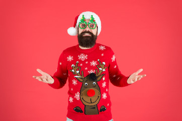Confused guy. Happy new year celebration. Join holiday celebration. Winter party outfit. Sweater with deer. Hipster bearded man wear winter clothes red background. Christmas celebration ideas