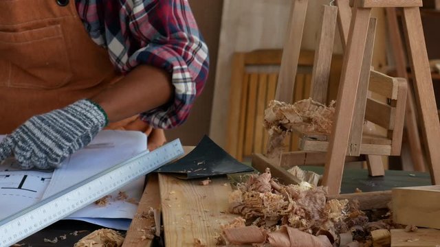 Old Asian craftsman touch his mouth and thinking about his process for working with wood product in the room during day time.