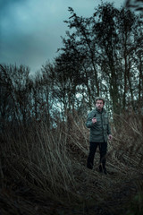 Man with pistol between reed on cloudy day.