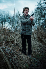 Man with pistol between reed on cloudy day.