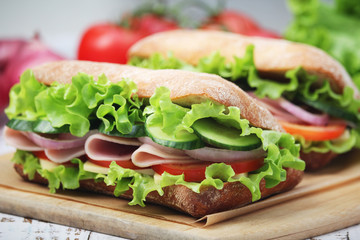 Two sandwiches with fresh vegetables, ham and cheese in ciabatta bread	
