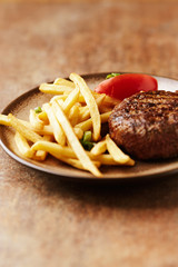 Hamburger steak with french fries and tomatoes. Brown stone background.