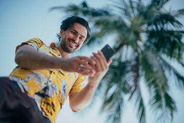 A contented man is standing with a phone in his hands on a background of palm trees.