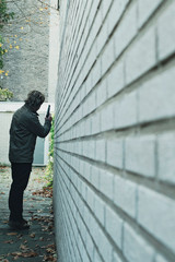 Man with pistol in alley along white brick wall. Rear view.