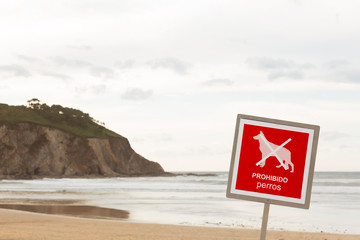Playa con cielo nublado con señal roja de advertencia donde se prohibe el baño a perros y animales