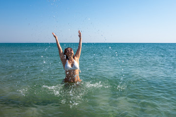 Woman with arms raised up in the sea making the water flow happily, drops falling down. Concept of joyfulness, positivity, optimism