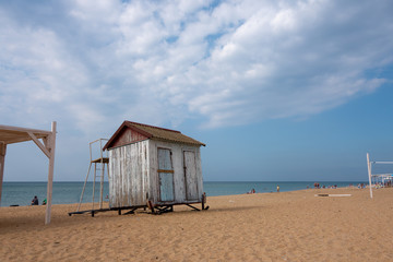 The empty beach on the sea in autumn with a small abandoned cloakroom. Cloudy sky in the afternoon