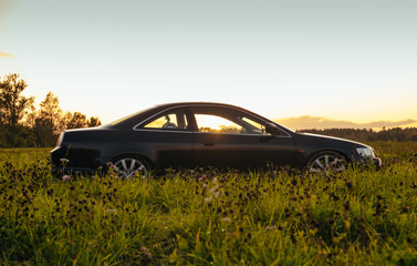 Black coupe car in green field sunset time