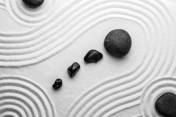 Schwarze Steine auf Sand mit Muster, Draufsicht. Zen, Meditation, Harmonie