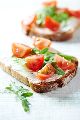 Tomato sandwich with cream cheese and fresh rocket on bright wooden background. Close up.