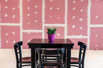 A black wooden table with a flower in a pink pot in the center and four chairs on a background of pink walls with a white pattern in a cafe, restaurant, diner or shopping center