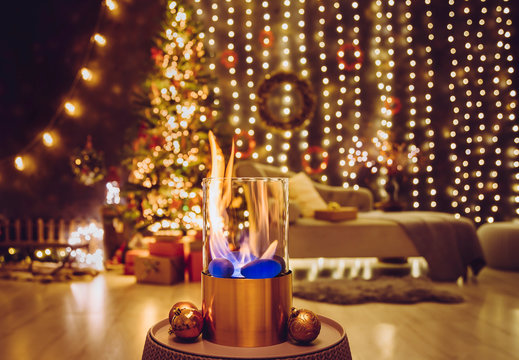 Selective Focus On Modern Freestanding Portable Glass And Copper Metal Fireplace Burning Bio Ethanol Gas On Living Room Table With Cozy Christmas Eve Home Decor Interior On Background.