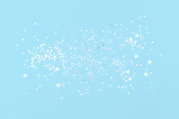 scattered white and light blue holographic glitter confetti star shaped on tender pastel blue background Flat lay top view copy space. Festive holiday backdrop. Birthday, giveaway, Christmas, New Year