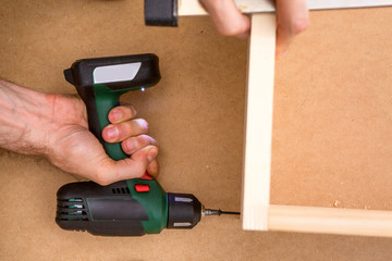 Drill driver whit screw on wooden background. Hand and screw gun or drill holding screw on wood. Making wooden furniture. 