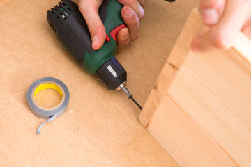 Drill driver whit screw on wooden background. Hand and screw gun or drill holding screw on wood. Making wooden furniture. 