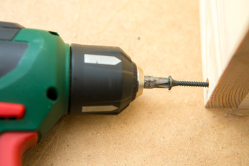 Drill driver whit screw on wooden background. Hand and screw gun or drill holding screw on wood. Making wooden furniture. 