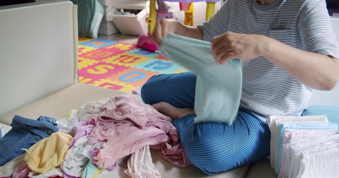 Asian Grandmother sitting and folding the baby girl clothes at home.people and kids clothing concepts.