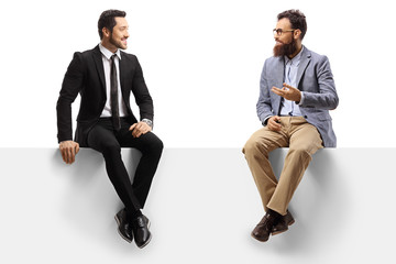 Man in a suit and a bearded man sitting on a blank panel and talking - Powered by Adobe