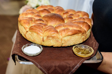 A woman holds a metal tray with fresh round bread and two plates of salt and honey. Bulgarian tradition, wedding.