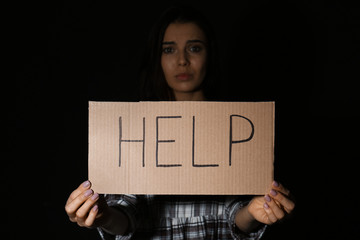 Abused young woman with sign HELP on black background. Domestic violence concept