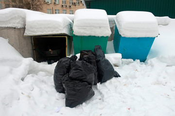 black garbage bags in a snowdrift in a garbage bin near garbage bins