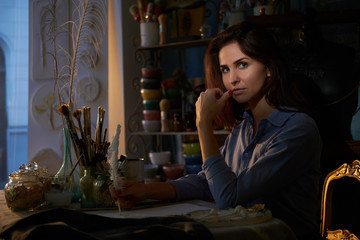 Beautiful creative woman is working on her new project at nicely decorated workshop.