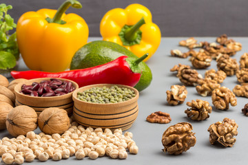 A set of products for diet food. On a gray background, walnuts, chickpeas, beans, lentils, yellow and red peppers, tomatoes, avocado.
