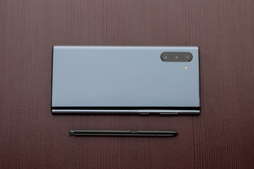 Smartphone with three cameras and a stylus on a wooden table close-up.