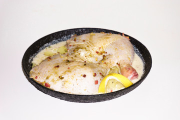 Two fresh chicken legs with spices and lemon in a black pan prepared for frying. Isolated on a white background. Asian and European cuisine.