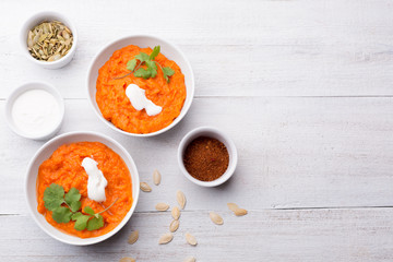 Pumpkin dish with sour cream, pumpkin seeds, cilantro and spices on a white wooden background.