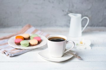 Morning coffee, breakfast, macaroons on a plate on white wooden table, close up.