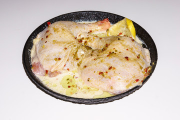 Two fresh chicken legs with spices and lemon in a black pan prepared for frying. Isolated on a white background. Asian and European cuisine.