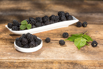 Ripe blackberries with leaves in a bowl on a woodenk background