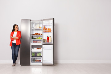 Happy young woman near open refrigerator indoors, space for text
