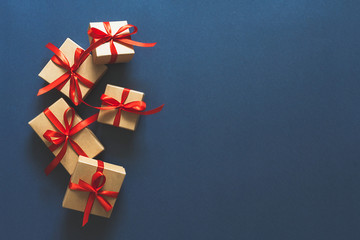Christmas flat lay. Holiday gifts in boxes in craft paper and a red ribbon on a classic blue...